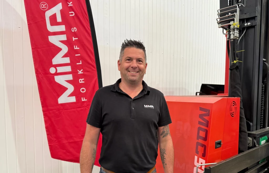 Alex Payne, Sales Director at MiMA Forklifts UK, standing beside a MiMA forklift in warehouse setting